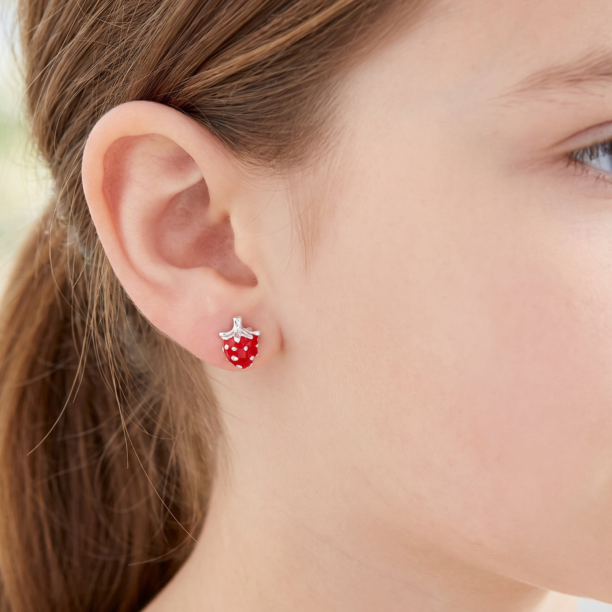 Close-up of a young girl wearing strawberry enamel children’s sterling silver earrings.