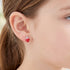 Close-up of a young girl wearing strawberry enamel children’s sterling silver earrings.