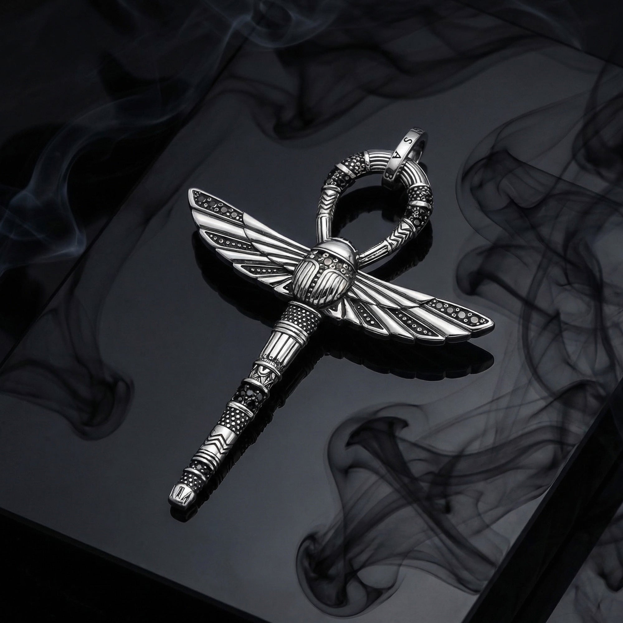 Thomas Sabo cross of life ankh scarab pendant laying on a dark mirrored surface surrounded by mystical black smoke.
