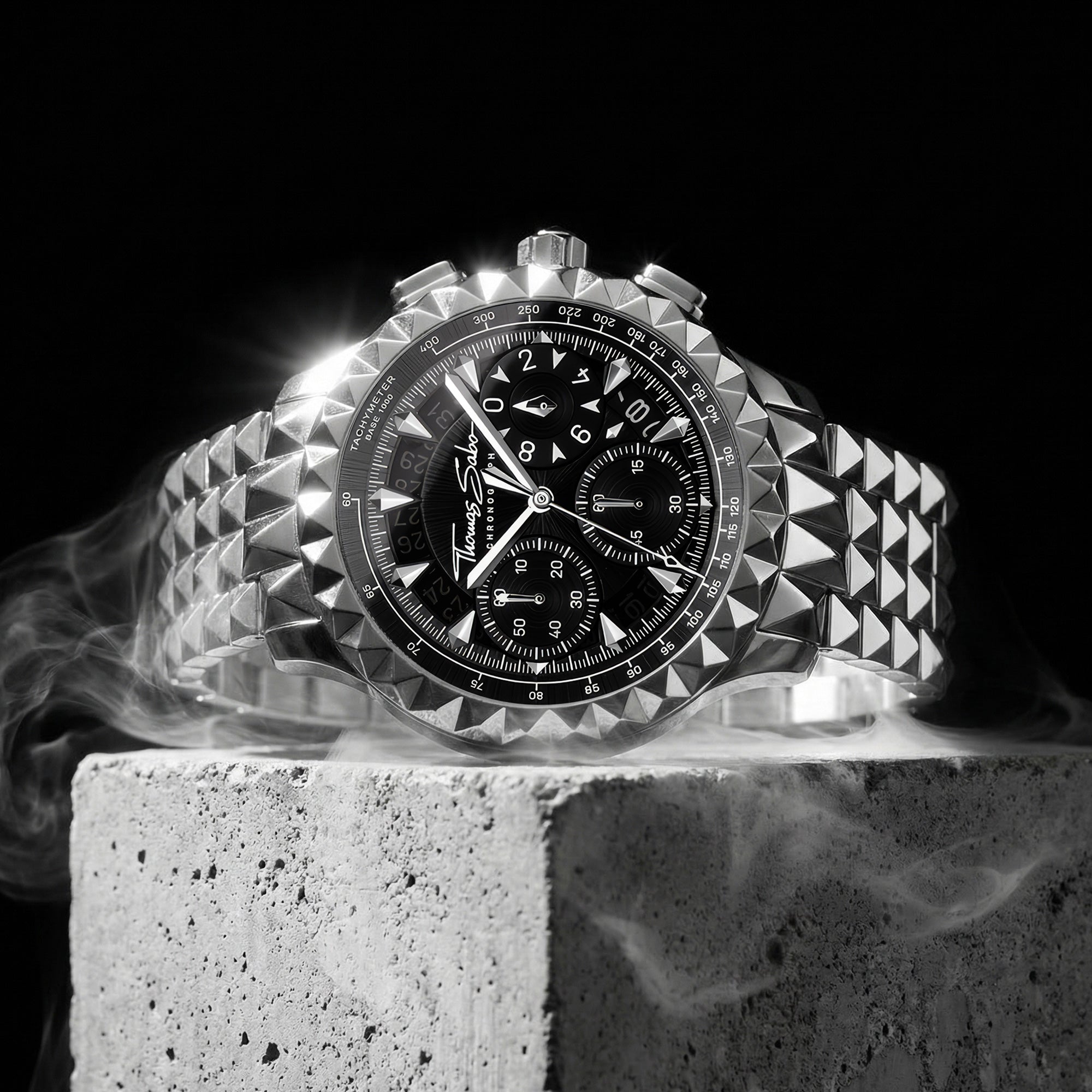 Thomas Sabo Rebel At Heart silver pyramid men's watch sitting on a concrete block with smoke rising from underneath.