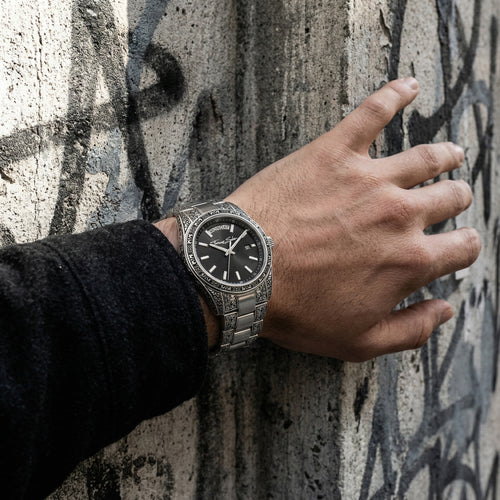 Man wearing a Thomas Sabo Rebel At Heart Revive 36mm black dial watch resin this hand on a concrete wall with graffiti. 