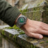 Man wearing a Thomas Sabo Rebel At Heart Revive 40mm green dial watch wresting his hand on the moss-covered block work of an old building.