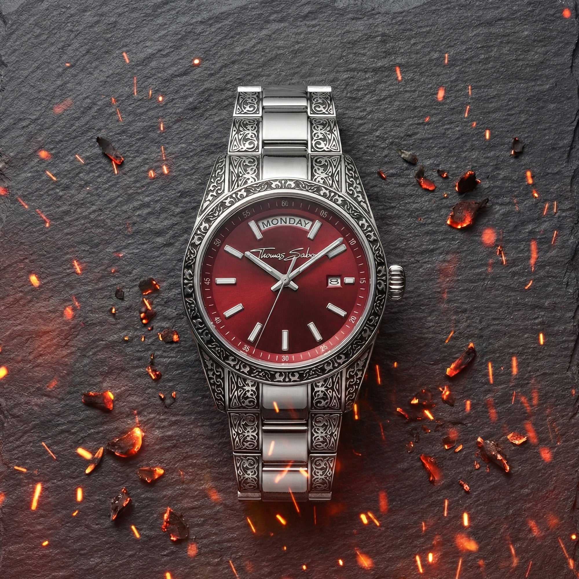 A Thomas Sabo Rebel At Heart Revive 36mm red dial watch on black slate surrounded by burning embers and sparks.