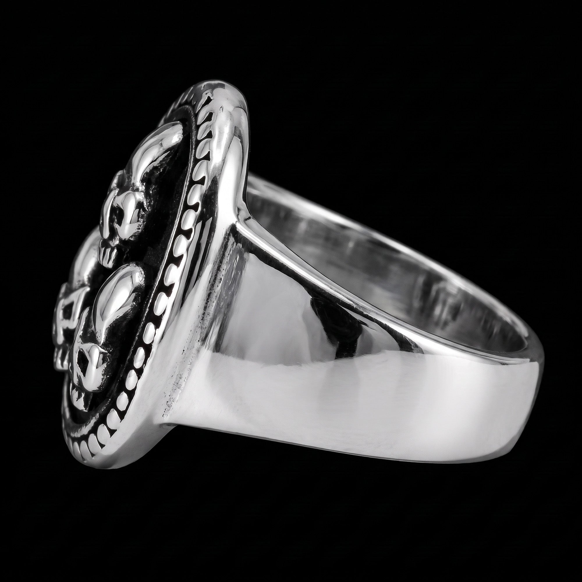 A three skulls stainless steel men's signet ring tilted to the left.