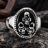 A three skulls stainless steel men's signet ring sitting on a broken rock with rusted iron remains in the background.
