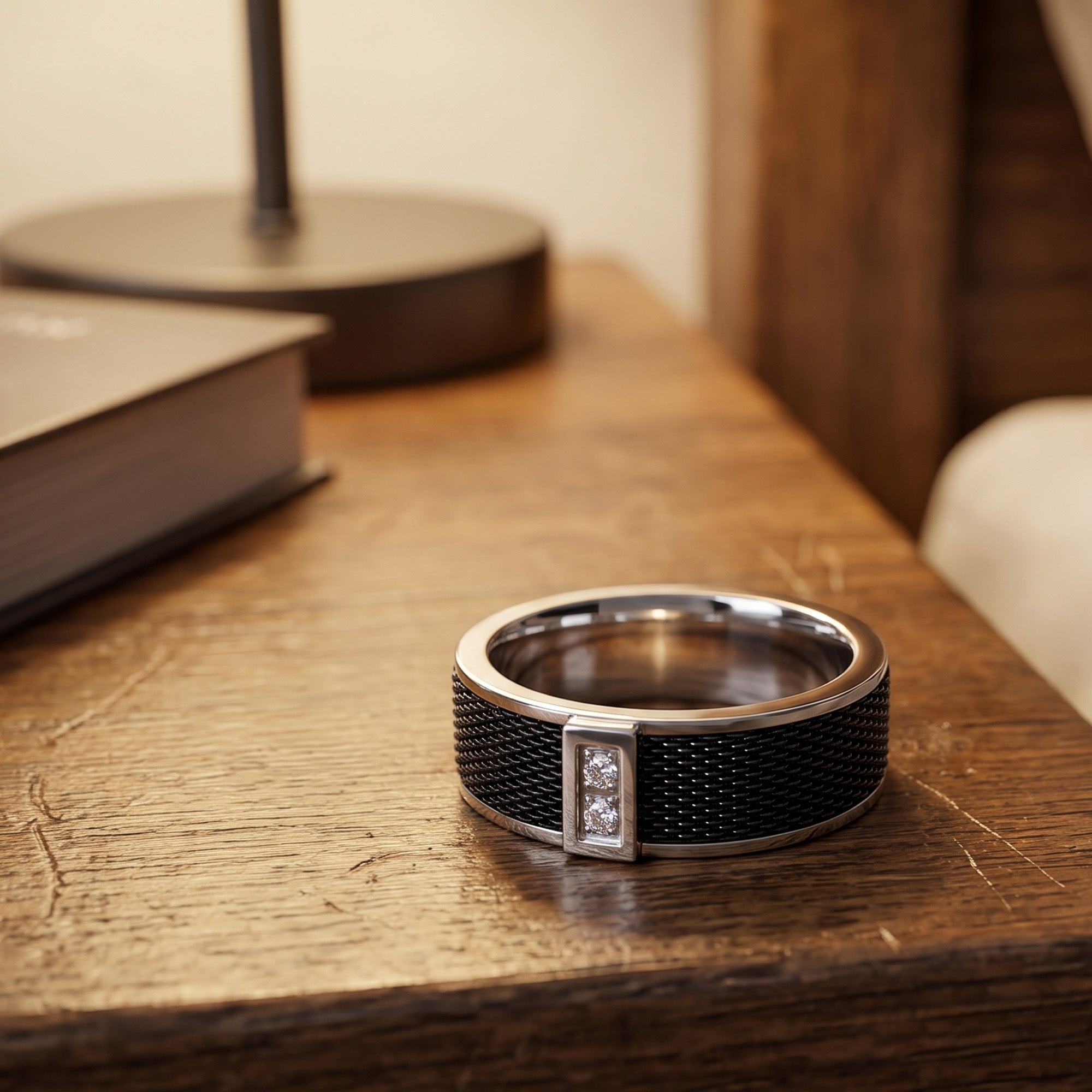 A titanium black mesh twin CZ men's ring on the edge of a wooden bedside table.