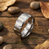 Titanium men's matte finish notched edge ring on a wooden surface surrounded by small rocks and leaves.