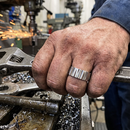 Man holding a spanner in a metal workshop wearing a titanium tapered groove matt finish ring.