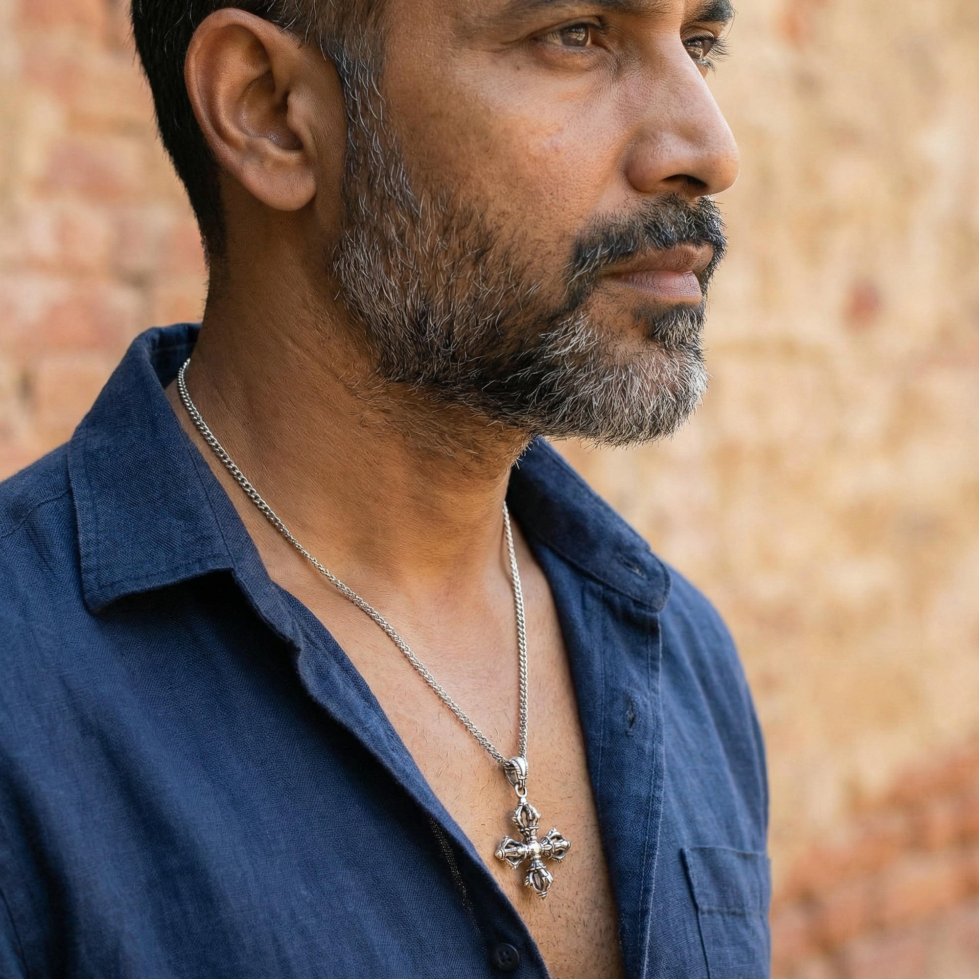 Bearded man in a blue open-neck shirt facing right wearing a vajra cross sterling silver necklace.