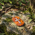 A cross wood inlay steel dog tag necklace laying on a moss-covered rock next to a tree in a forest.
