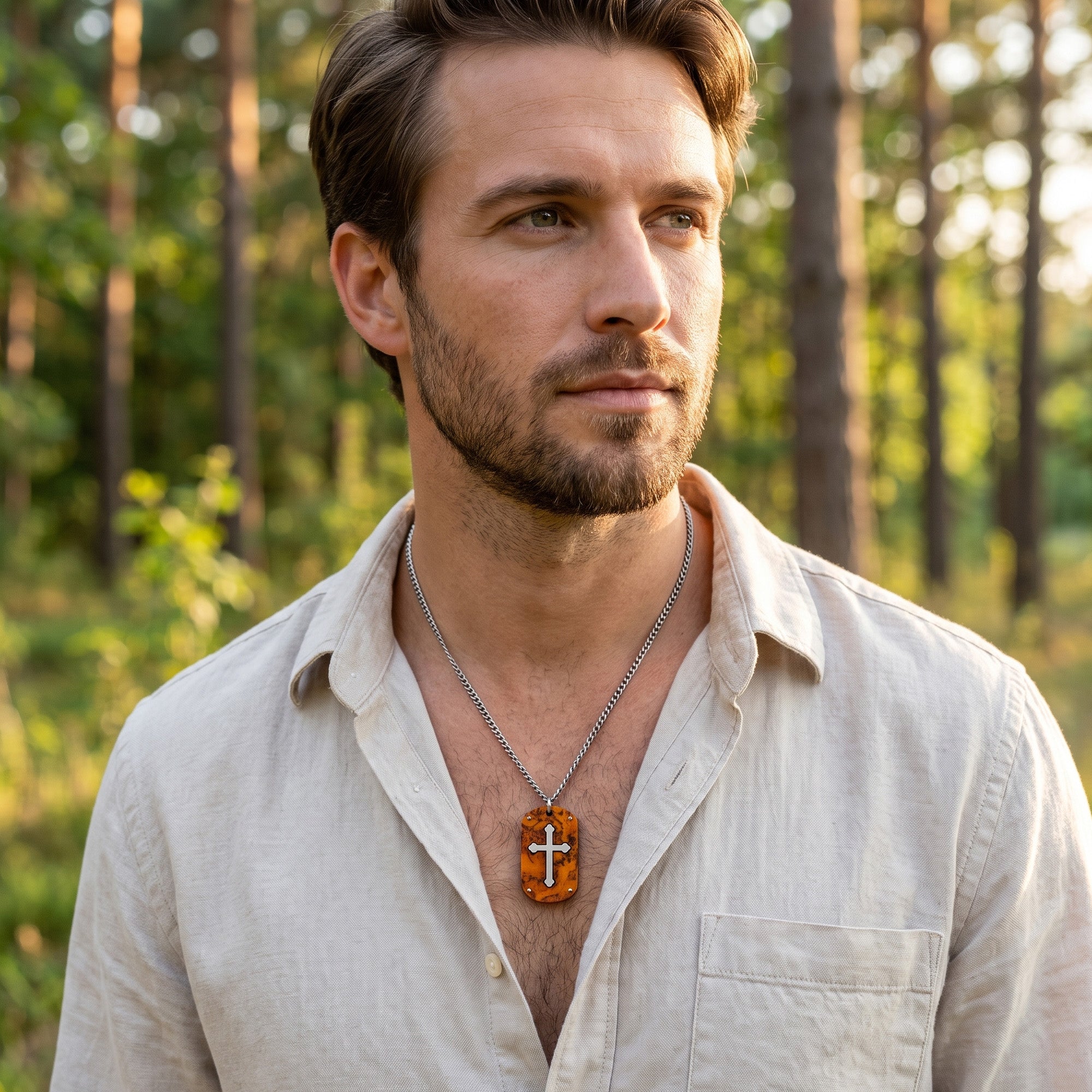 A man standing in a wooded clearing in an open-neck shirt wearing a cross wood inlay steel dog tag necklace.